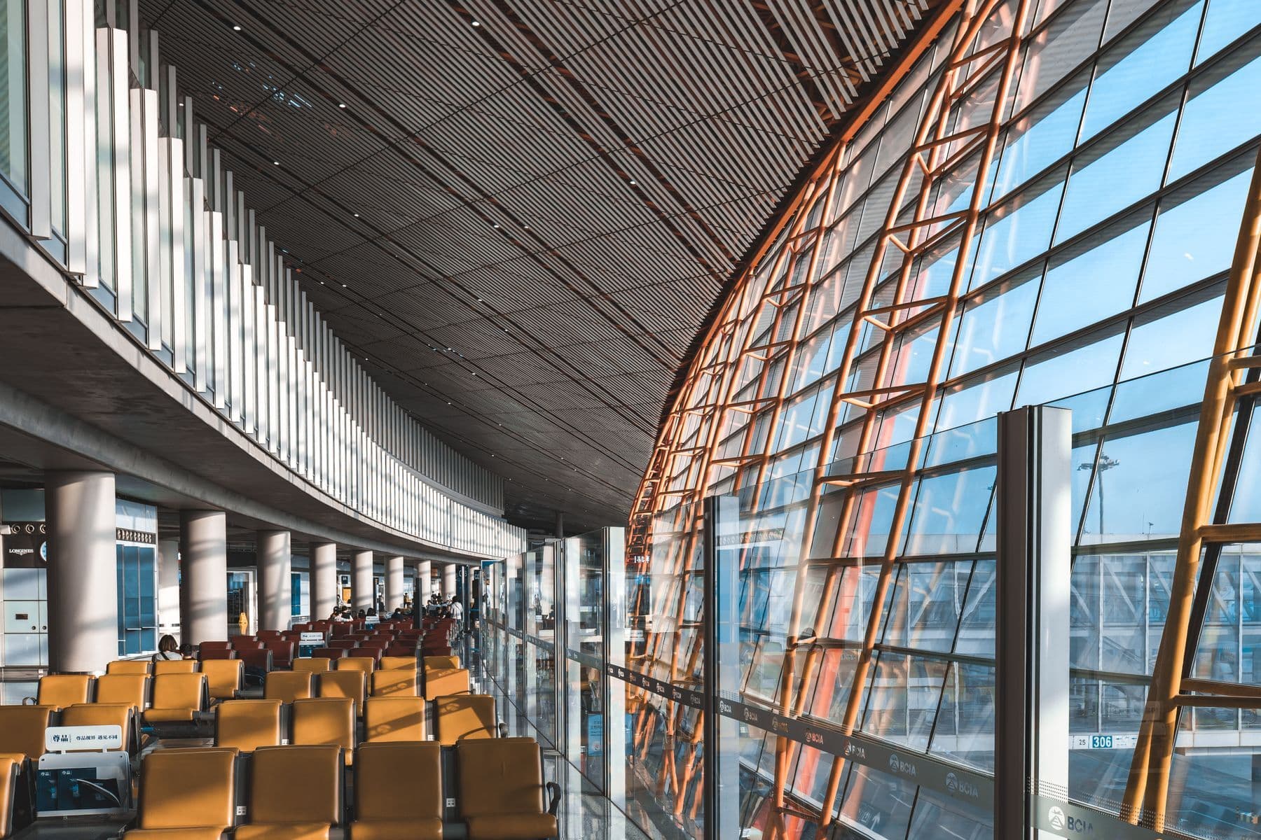 A long airport concourse with rows of yellow seats beside a curved glass wall.