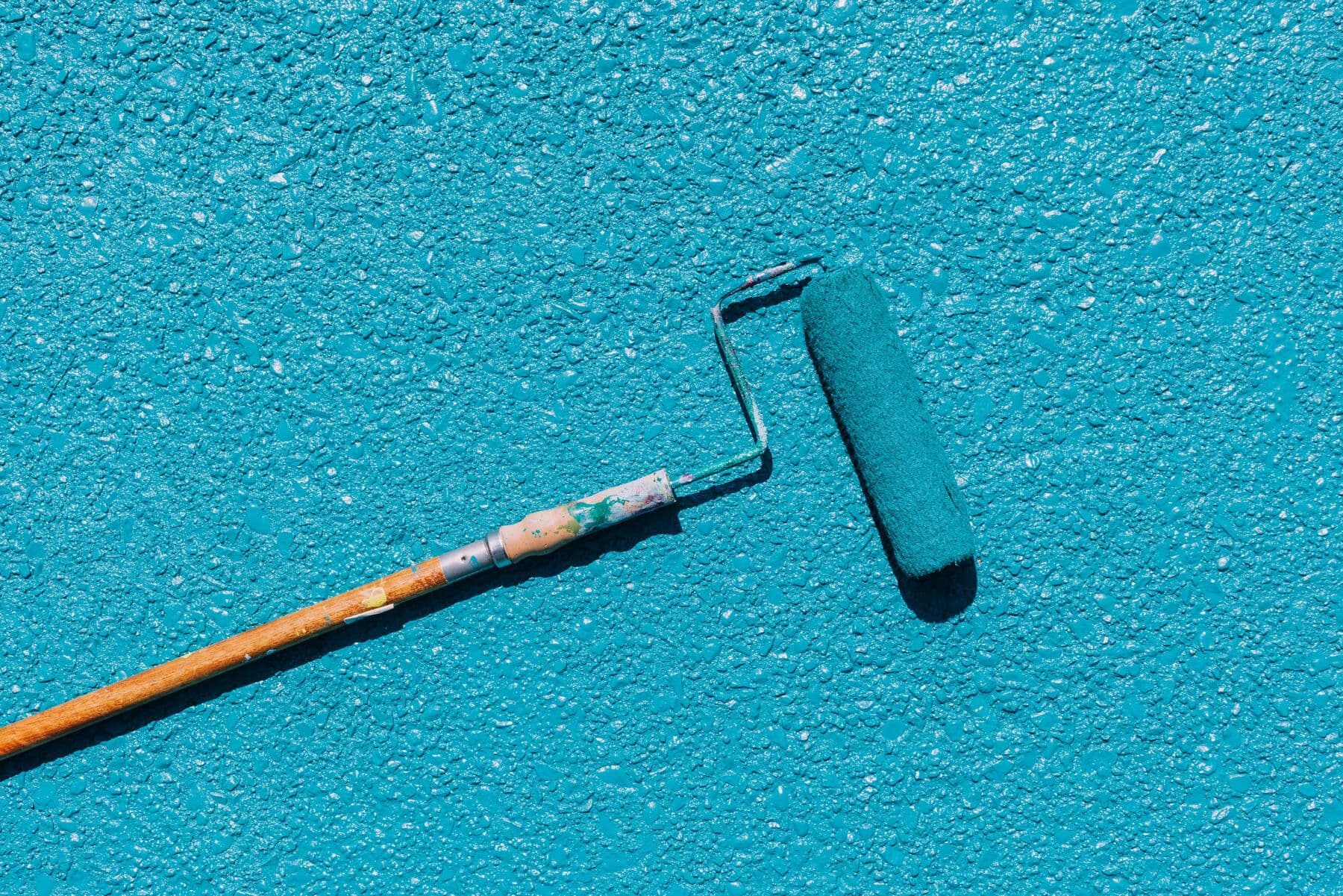 A paint roller lying against a textured blue wall.