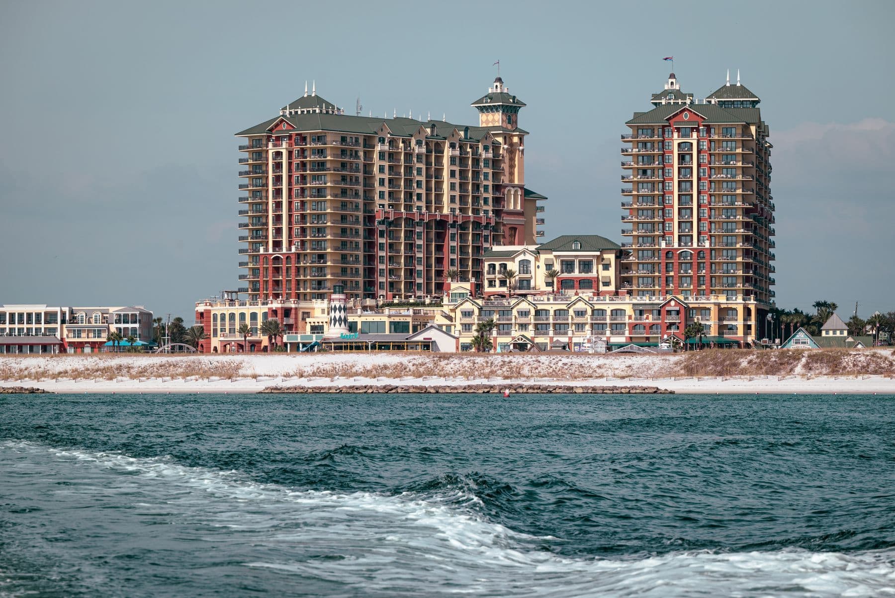 Two beachfront high-rise towers and a low shopping village seen from the water.