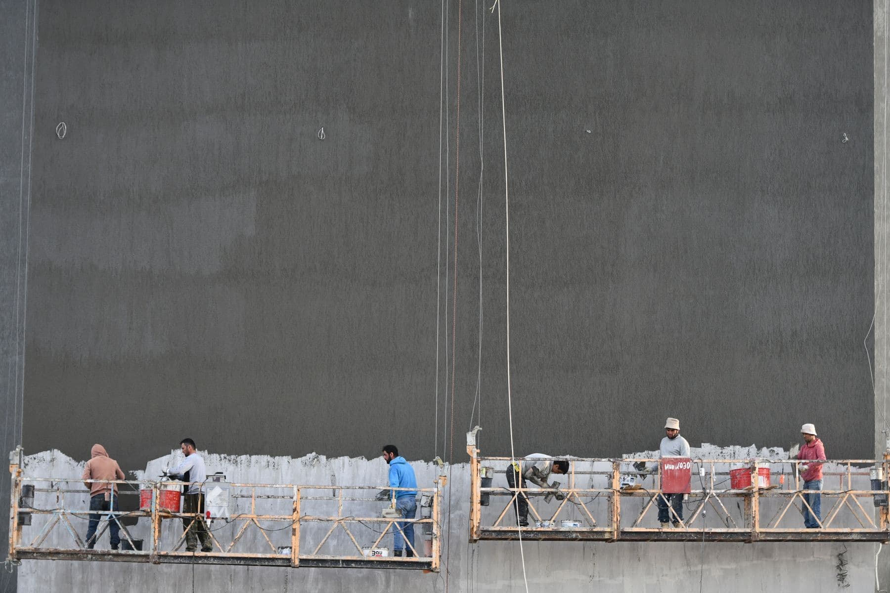 Workers on two suspended platforms along the dark face of a tall building.