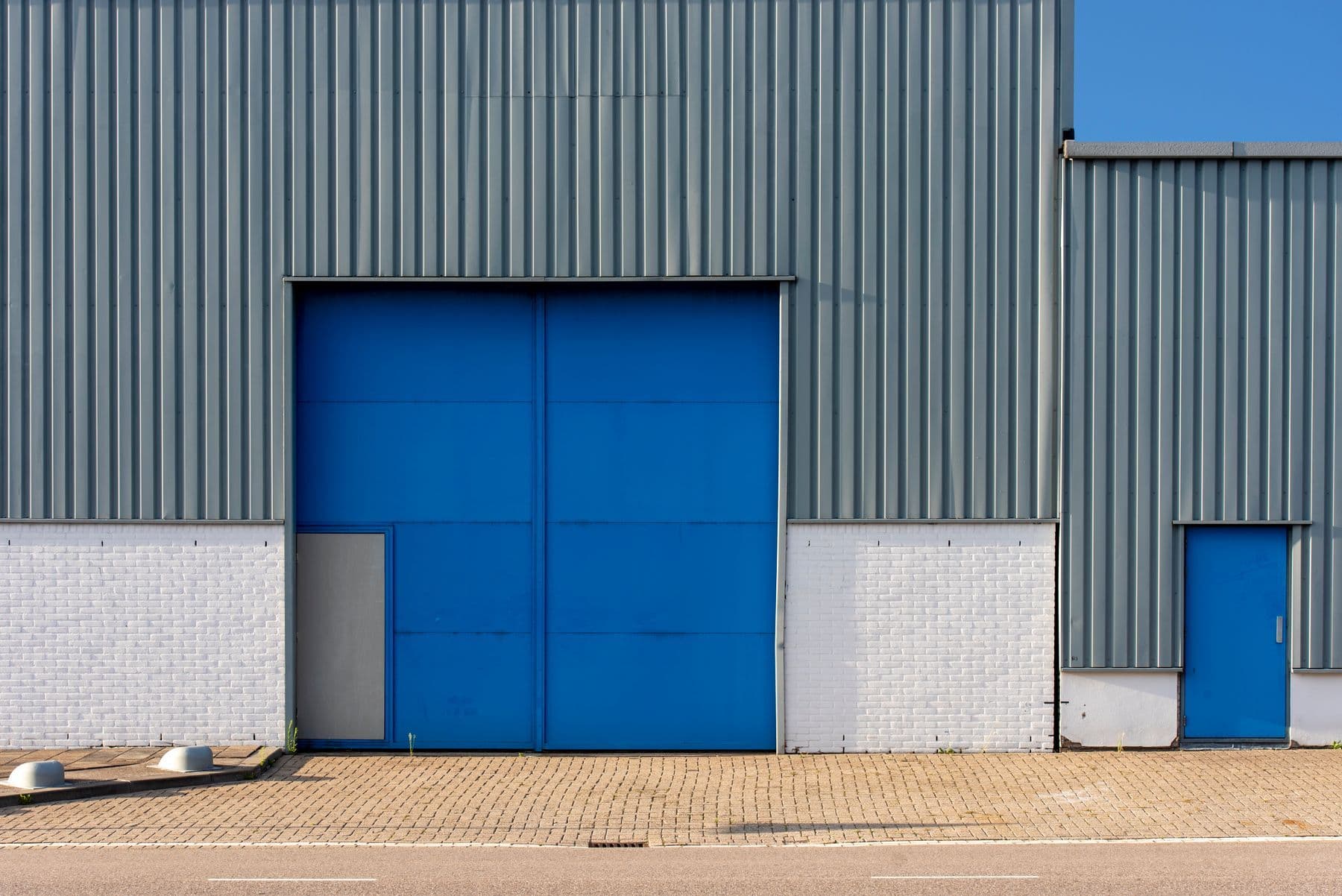 A gray metal warehouse with a white block base and a large blue loading door.